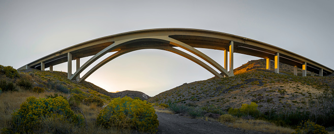 Futuristic arching bridge over the arid desert landscape at sunset