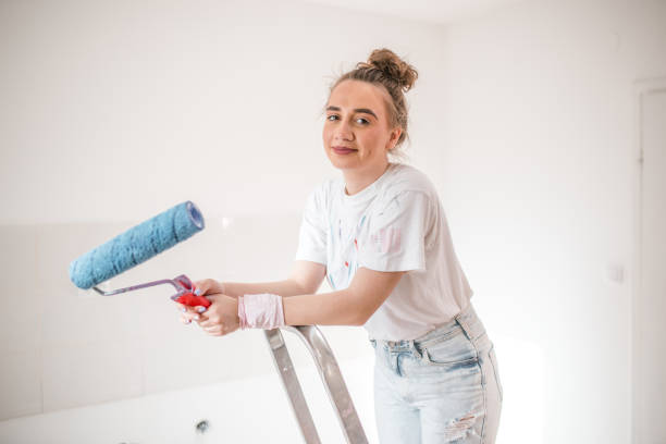 istock Side view of a woman standing on a ladder holding a paint roller 1433012704