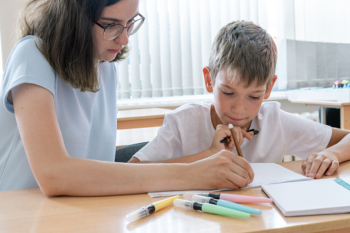 A boy and a teacher doing homework, writing text in a notebook at the table. A mother helps her son write in a notebook. The babysitter helps to complete school assignments. back to school
