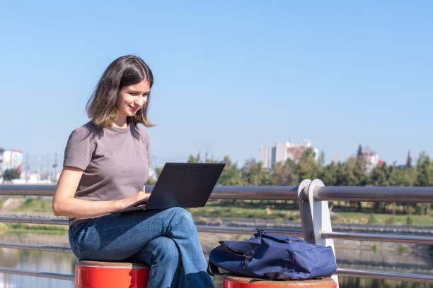A beautiful brunette student with glasses is using a laptop on the street. A beautiful student girl uses a laptop