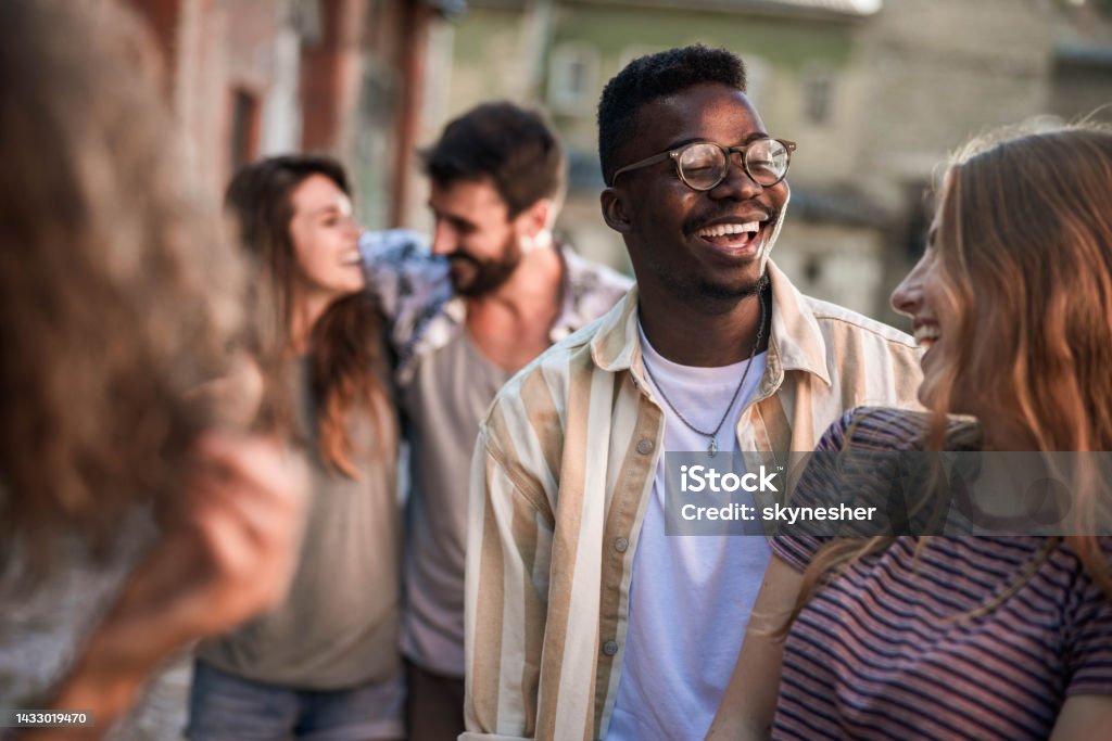 Happy couple talking among their friends on the street. Happy black man talking to his white girlfriend while being among their friends on the street. Adult Stock Photo