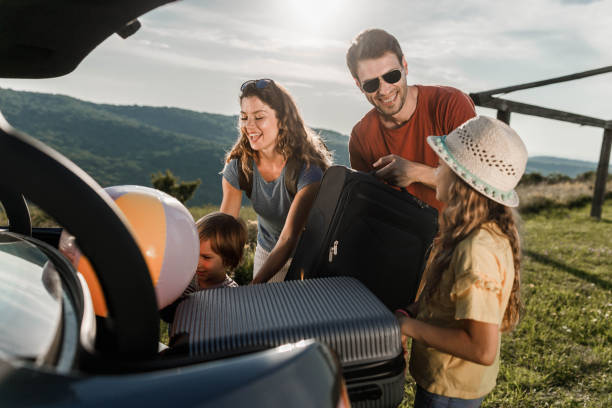 istock Happy family talking while packing their luggage into a car trunk. 1433020219