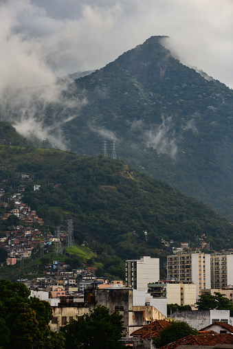 The cloud-shrouded Andaraí Maior peak and the Atlantic rainforest of Tijuca National Park towering above favelas and neighboring districts of the Zona Norte, or North Zone of Rio de Janeiro, Brazil