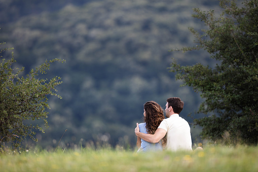 Rear view of a loving couple embracing while relaxing in grass and looking at view. Copy space.