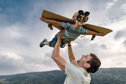 Happy single father having fun while holding his boy high-up while he is pretending to be an airplane. Copy space.
