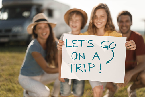 Happy family is ready for their summer trip while focus is on girl's hand holding paper with a text 'Let's go on a trip'.