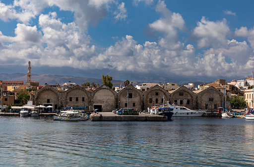 Chania, Crete, Greece - August 25, 2022: Boats and yachts moored in the Venetian Harbor in Chania, Crete. Venetian dockyards in the background.