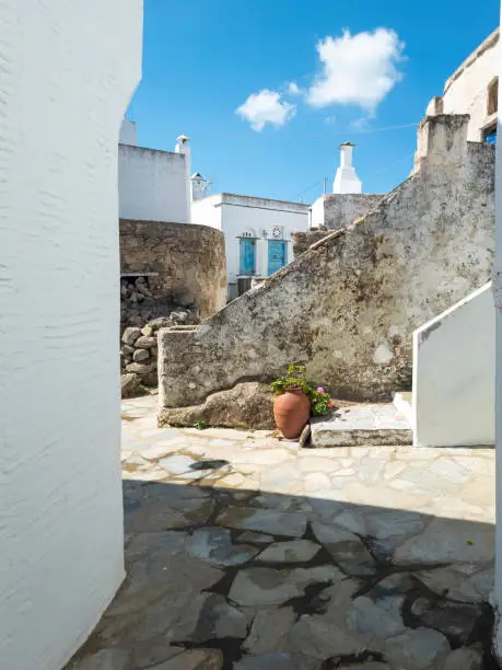 Greece, Cyclades. Tinos island, Volax village. Old stone walls between whitewashed buildings, paved alleys under Greek blue sky. Vertical