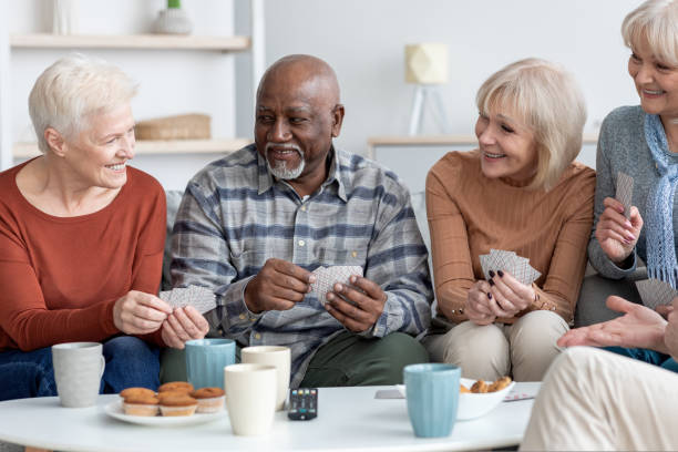 grupo internacional de ancianos alegres que se relajan juntos, jugando a las cartas - senior living communitiy fotografías e imágenes de stock