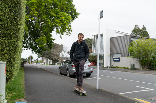Tauranga New Zealand - October 12 2022;  Person on scooter commuting to work along a city suburban footpath.