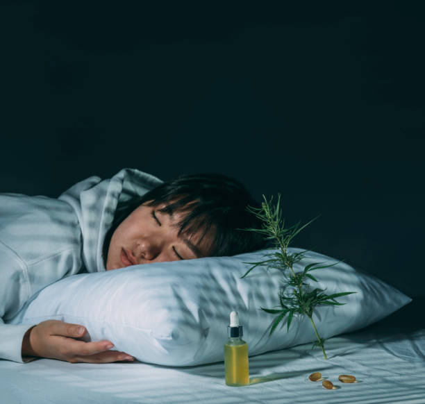 chica asiática durmiendo en el dormitorio de la noche con aceite de cbd, cápsulas y una rama de cannabis. producción de melatonina, concepto de combatir los trastornos del sueño. fondo oscuro - narcotic medicine pill insomnia fotografías e imágenes de stock