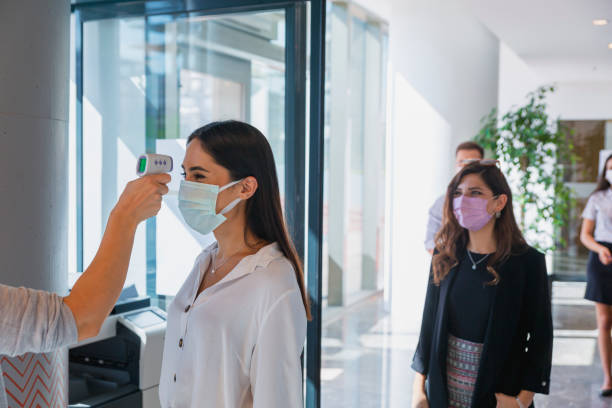 impiegato che misura la temperatura degli uomini d'affari con maschera facciale per la pandemia mentre i colleghi tornano in ufficio - infrared thermometer foto e immagini stock