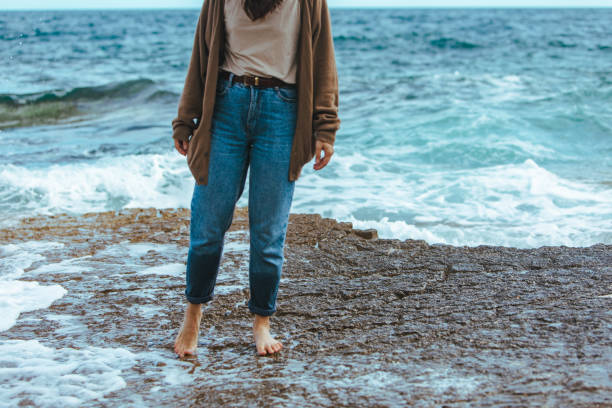 woman walking by rocky beach barefoot wet jeans summer vacation