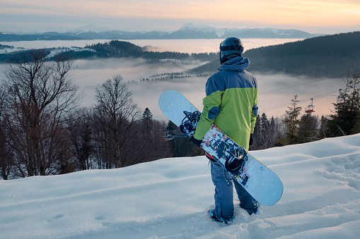 man snowboarder enjoying the view of sunset above the snowed mountains winter travel concept
