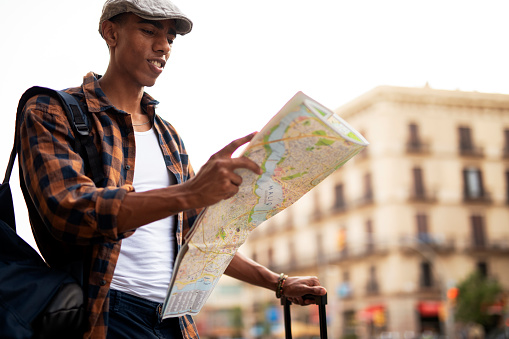 Happy young man with a city map. Young handsome male traveler, standing on the street and looking at the map