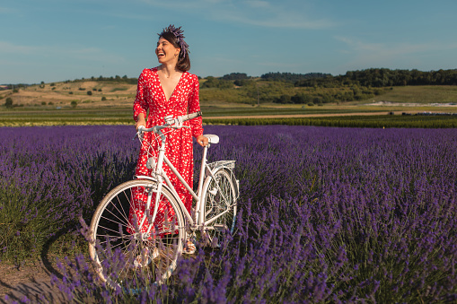 a young woman in a red dress stands with white bicycle in a lavender field