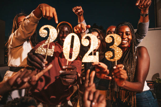 Group of friends celebrating 2023 New Year's Day holding numbers during a rooftop party stock photo
