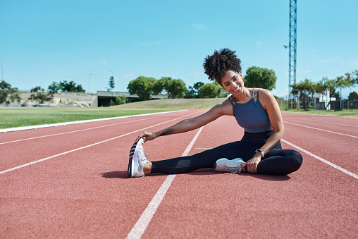 Workout, fitness and black woman stretching before run on outdoor track, cardio and energy training. Sports, running and exercise by healthy lady warm up exercises, sitting and prepare for practice