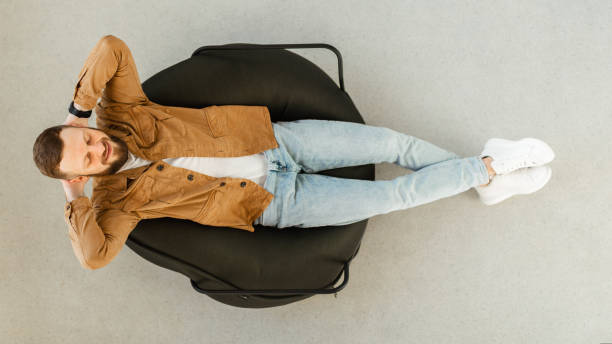 Happy Guy Relaxing With Eyes Closed In Chair At Home Happy Bearded Guy Relaxing With Eyes Closed Sitting In Chair At Home. Lazy Contented Male Resting And Sleeping Holding Hands Above Head Enjoying Domestic Weekend. Top View, Panorama man sleeping chair stock pictures, royalty-free photos & images