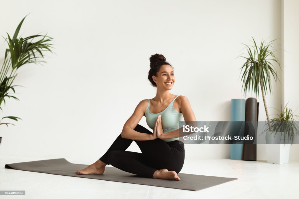 Portrait Of Beautiful Young Female Making Yoga Practice In Light Studio Portrait Of Beautiful Young Female Making Yoga Practice In Light Studio, Happy Smiling Millennial Woman Sitting On Fitness Mat And Doing Pilates Exercises, Enjoying Healthy Lifestyle, Copy Space Yoga Stock Photo