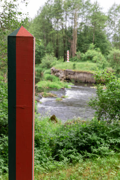 Border poles on the border line between Poland and Belarus on the Svisloch river. Vertical shot. Focus on belorussian border pole.