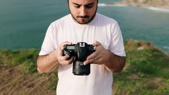 A young man outdoors with a DSLR camera in his hands