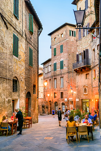 Siena, Tuscany, Italy, July 07 -- Some tourists enjoy life, a summer evening and the pleasures of Italian cuisine in a characteristic tavern along the alleys of the historic and medieval heart of Siena, in Tuscany. Siena is one of the most beautiful Italian cities of art, in the heart of the Tuscan hills, famous for its immense artistic and historical heritage and for the Palio, one of the oldest and most exciting horse races in the world. Every year the seventeen villages of the city compete during the Palio in Piazza del Campo, an ancient medieval square famous for its shell shape. Since 1995 the historic center of Siena has been declared a World Heritage Site by UNESCO. Image in high definition format.