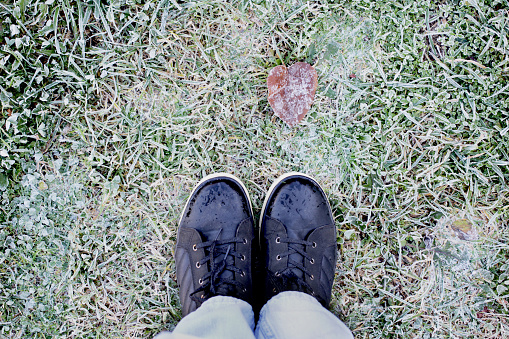 Feet in black boots and blue jeans on the grass covered with frost on the first cold day of autumn top view