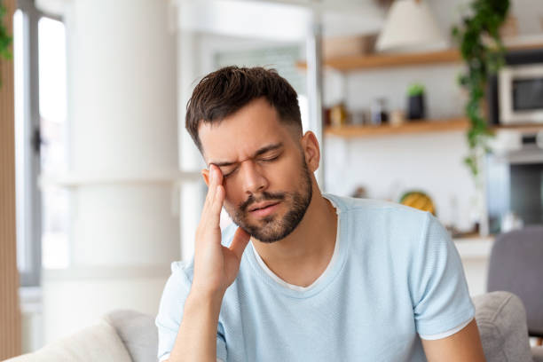 istock Man at home having a headache. Young man suffering from headache after hard working day, sitting on couch at home 1433045127