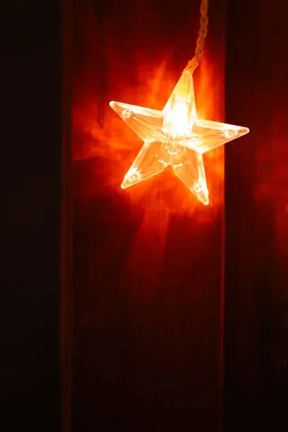Christmas.Star burning on a brown wooden background in warm colors.Festive glowing garlands on a dark background.