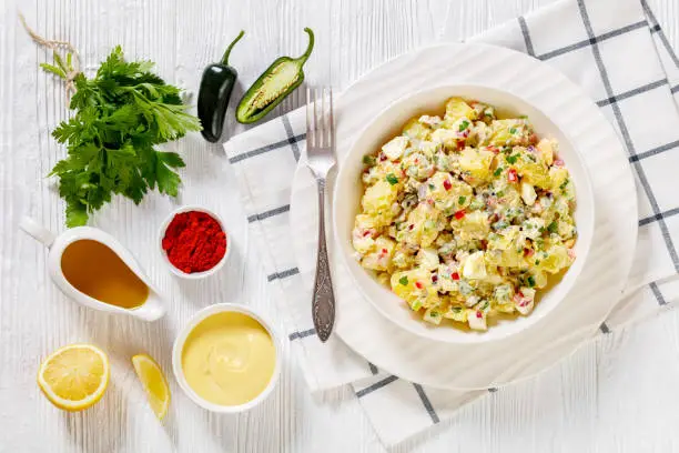 shout hallelujah potato salad with pickles, celery, eggs, jalapeno and mayonnaise dressing in white bowl on wooden table with ingredients, american cuisine, horizontal view from above, flat lay