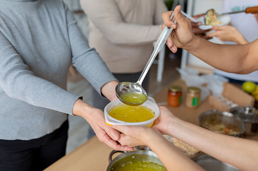 Help for aged people. Young volunteers serving hot soup for elderly or homeless in community charity donation center, closeup. Millennials helping with food to alleviate hunger
