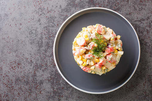 Salad with crab meat, corn, red onion, hard-boiled eggs and dill closeup in the plate on the table. Horizontal top view from above