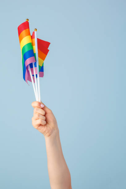 istock Closeup of a hand waving a small rainbow flag against a light blue background 1433052165