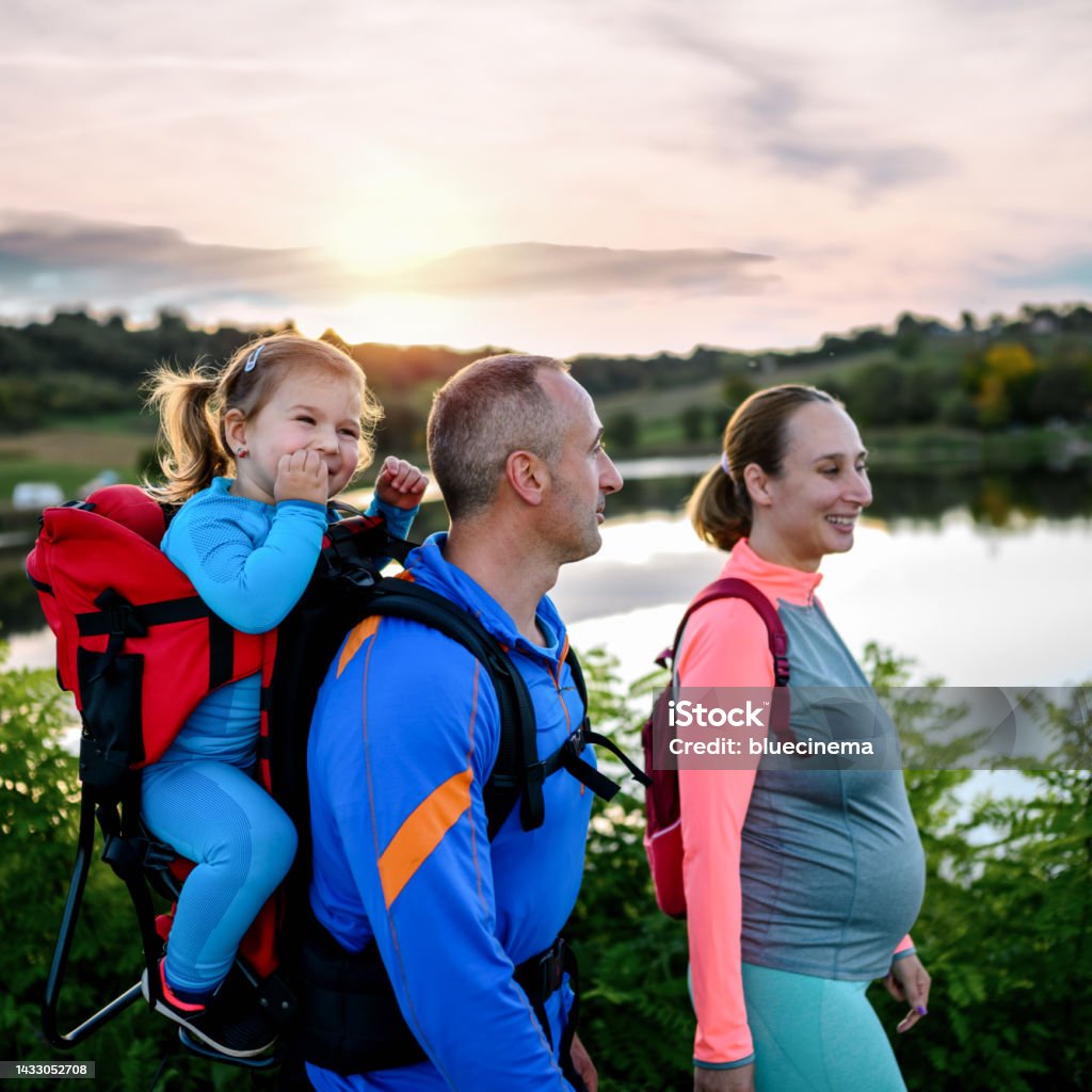 Active young family walks in nature. Active young family walks in nature. Daughter sitting in a carrier on her father's back Baby Carrier Stock Photo