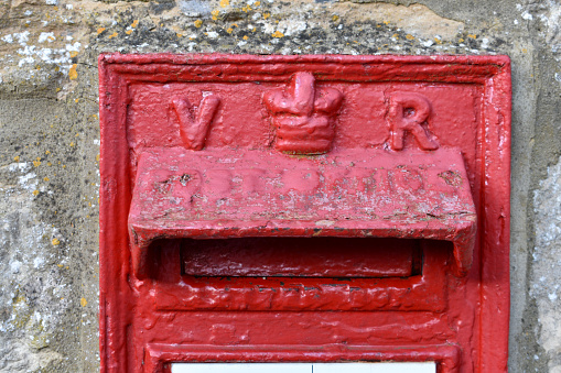 close up of red painted British Royal Mail letter box outside in a street,  showing the Queens crown and initials V R.  T