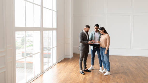 istock Couple Buying New Apartment, House Agent Showing Documents Blueprints 1433057387