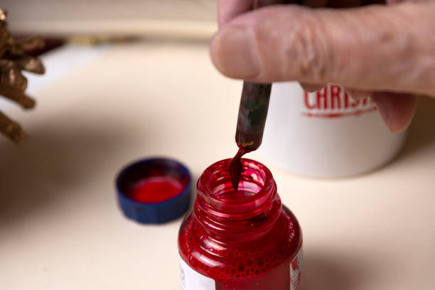 赤いインク瓶からペンに赤いインクを積み込む年配の男性の手のクローズアップ。手書きによる英語書道の概念。 - inoki antonio ストックフォトと画像