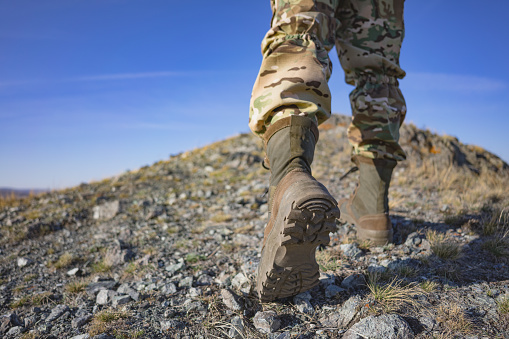 A soldier in camouflage and military boots climbs a mountain. Space for text. Shallow depth of field.