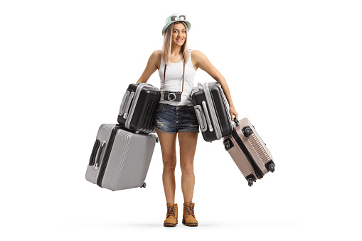 Full length portrait of a young female tourist holding many suitcases isolated on white background
