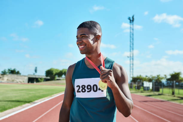 zwycięzca, medal i biegacz w wyścigu sportowym czarnego mężczyzny z uśmiechem za osiągnięcia w wyczynowych ćwiczeniach fitness. szczęśliwy wysportowany afroamerykanin w sporcie biegowym świętujący zwycięstwo na stadionie - medal 20s achievement athlete zdjęcia i obrazy z banku zdjęć
