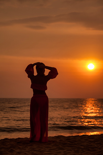 Mysterious silhouette middle aged woman dancing on tropical sea sunset. Female relaxing on summer beach at tropical background. Lady in beachwear long dress. Travel vacation concept. Copy text space