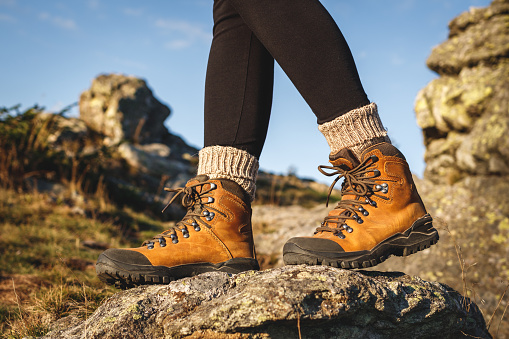 Leather hiking boot. Trekking in mountains. Female legs walking on rock