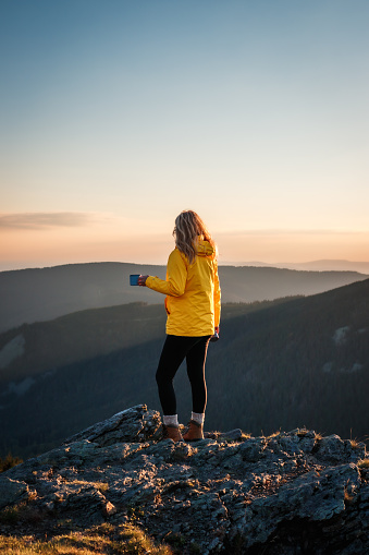 Woman traveler drinks coffee after successful hiking to mountain peak. Female hiker enjoying sunset over mountain range. Adventure in nature