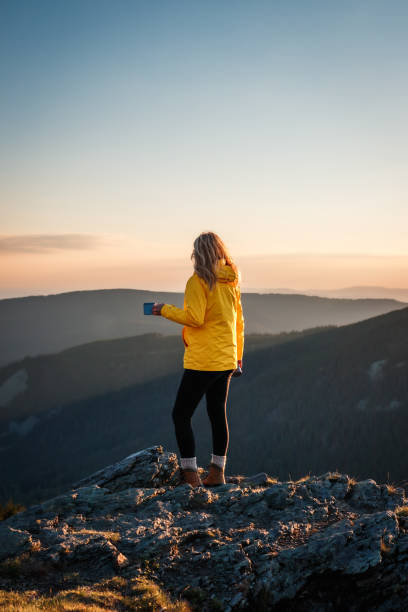 Woman traveler drinks coffee after successful hiking to mountain peak stock photo