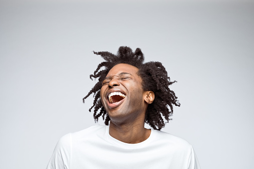Happy afro american young man wearing white t-shirt, laughing with eyes closed. Studio shot on grey background.
