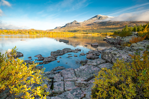 Mountain and sky reflecting in lake in early morning of autumn. Autumn colors in remote arctic landscape. Nieras mountain reflects in Lulealven dam in Stora Sjofallet national park, Sweden
