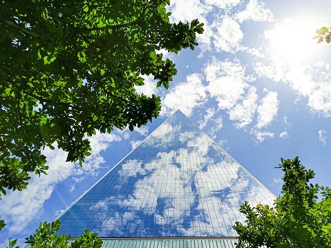 A low angle shot of the Walter Pyramid reflecting cloudy blue sky against green trees in Long Beach, California