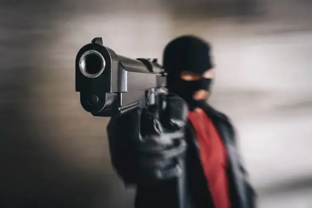 shooter in black mask attacks. Armed terrorist, thief with pistol in hands. criminal targeting with gun. Mafia gangster point gun in camera. Focus on pistol barrel. concept of banditry theft crime