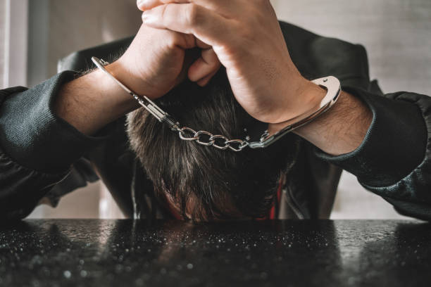 istock dangerous criminal is handcuffed in prison for interrogation. A repentant sad man with his head on the table. Arrest of a bandit. 1433069504